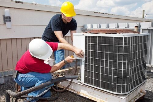Two technicians in hard hats servicing a rooftop condensing unit