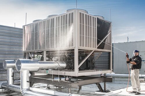 Technician pressure-washing the coil face of a rooftop chiller